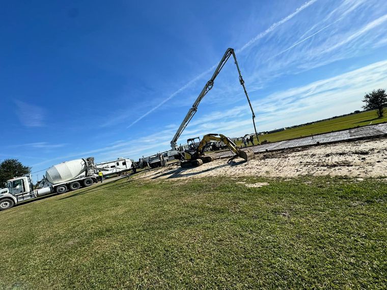 Construction site with concrete trucks and a pump pouring cement on a roadway under a blue sky.