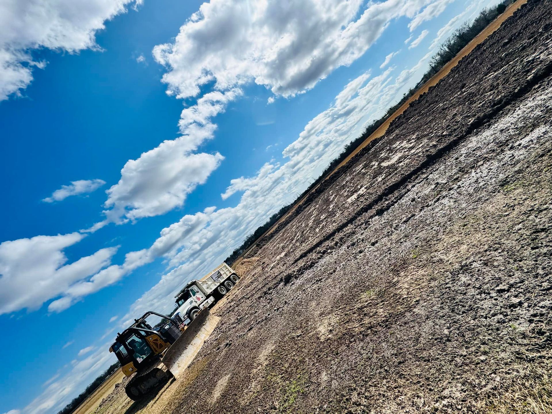 A bulldozer and truck on a field under a blue sky with clouds.