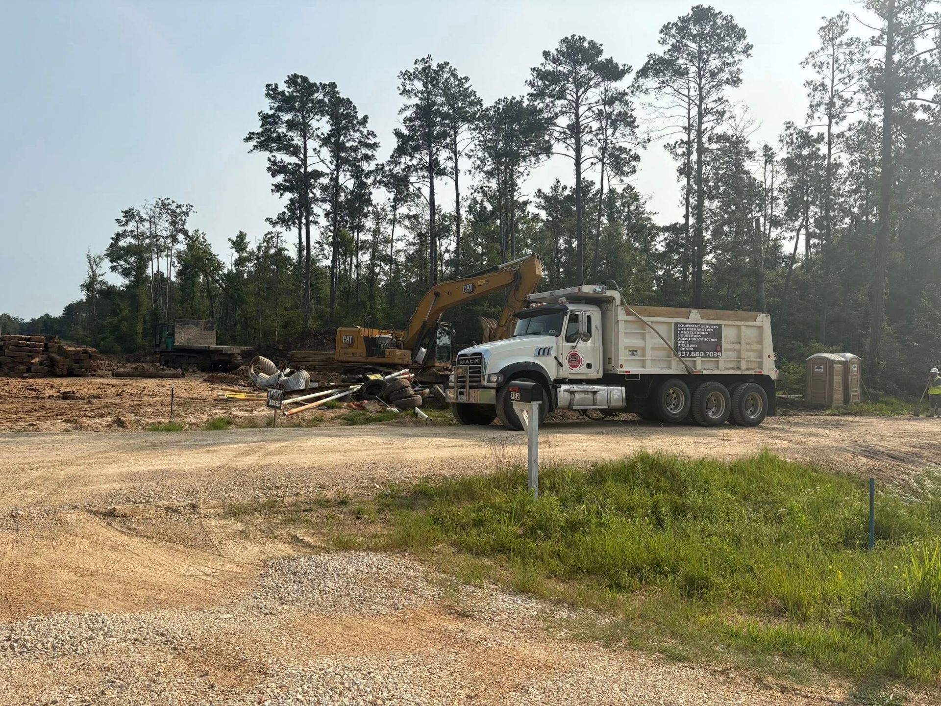 Construction site with a dump truck and excavator; trees in the background.