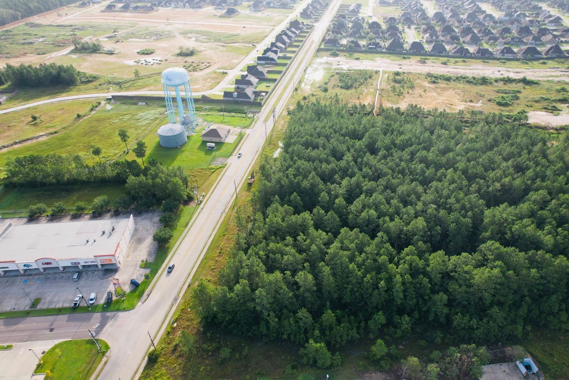 Aerial view of road through a suburban area with forest on the right. A water tower is in the center.