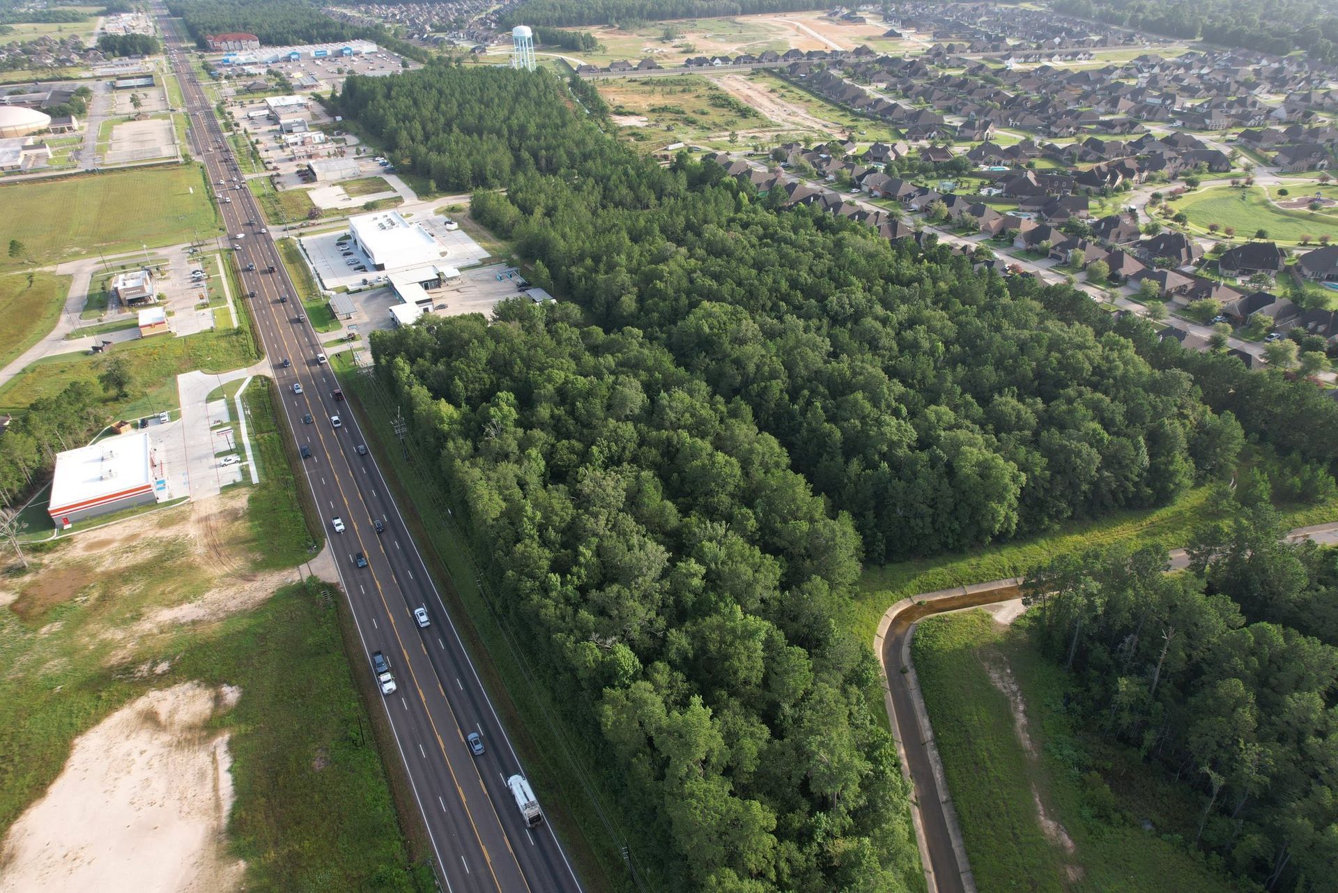 Aerial view of a highway with commercial buildings on one side and a large forest on the other.
