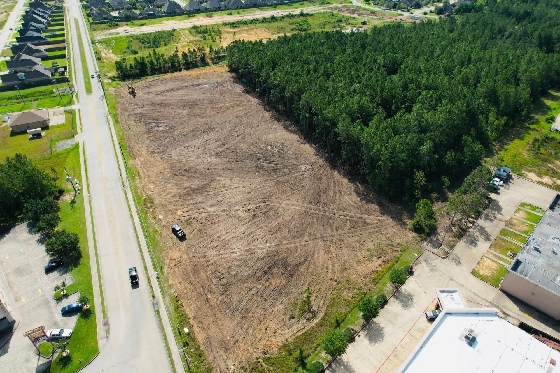 Aerial view: large cleared plot of land next to a forest and road, ready for development.