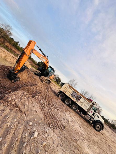 Orange excavator loading a dump truck with dirt on a construction site. Blue sky in the background.