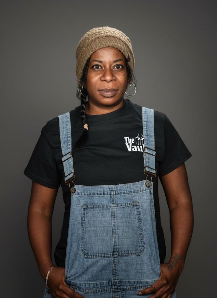Person wearing overalls and a beanie, posing with hands in pockets.