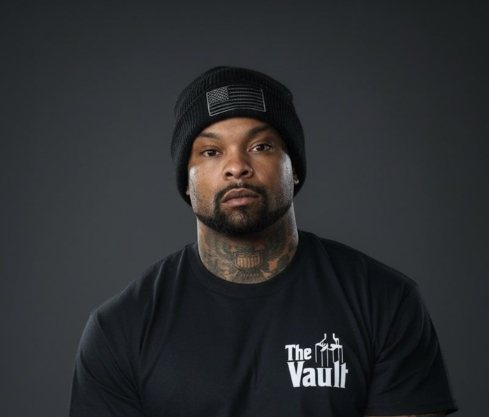 Man with tattoos, black beanie, and black t-shirt that says 