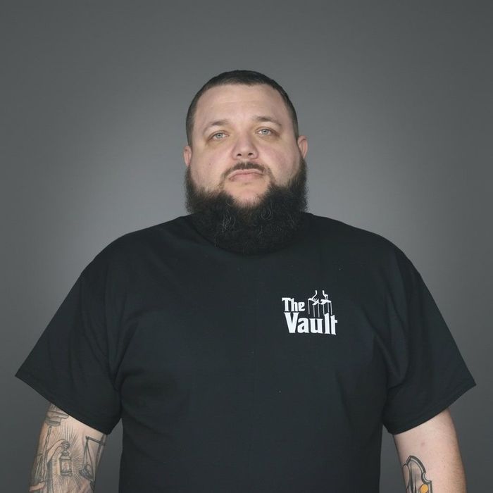 Man in black t-shirt with beard, tattoos, and logo 