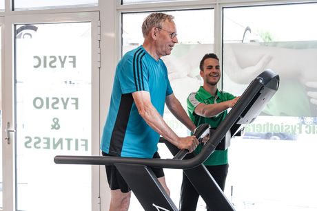 Een man loopt op een loopband met een personal trainer.