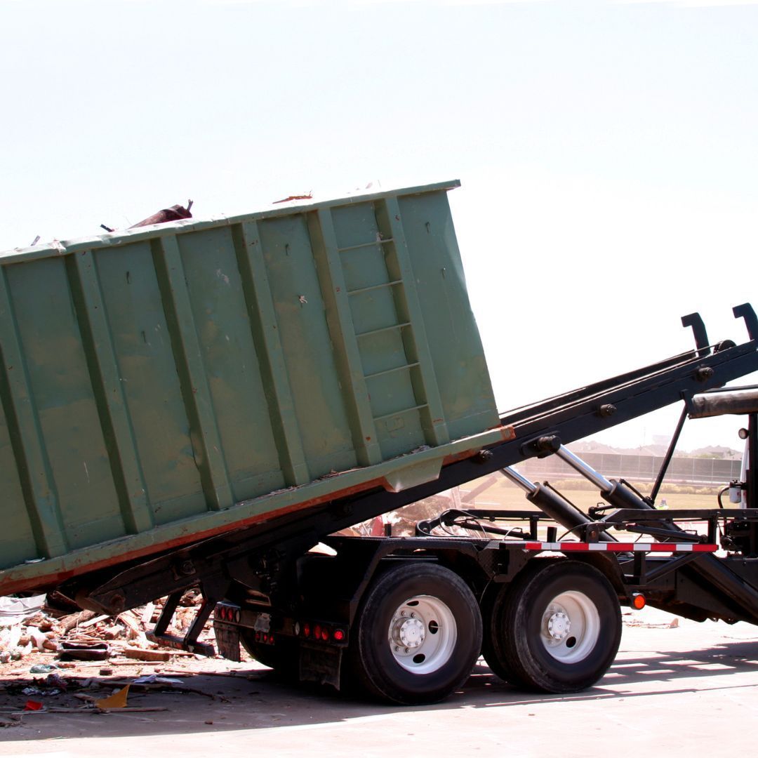 Overturned green dump trailer on a flatbed tow truck, debris scattered on the road