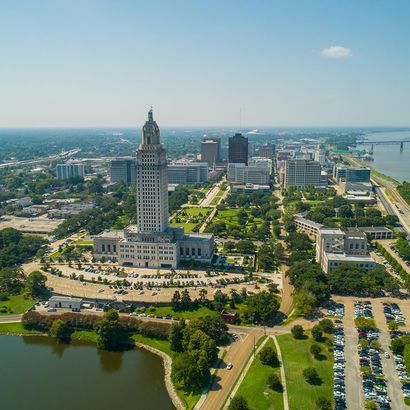 Aerial view of a city skyline with a tall tower, green park, and river under a clear blue sky