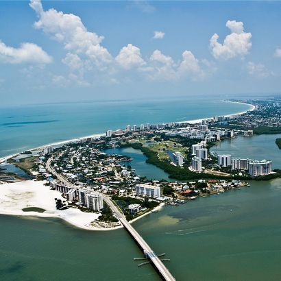 Aerial view of a coastal city with turquoise water, white sand, bridges, and high-rise buildings.