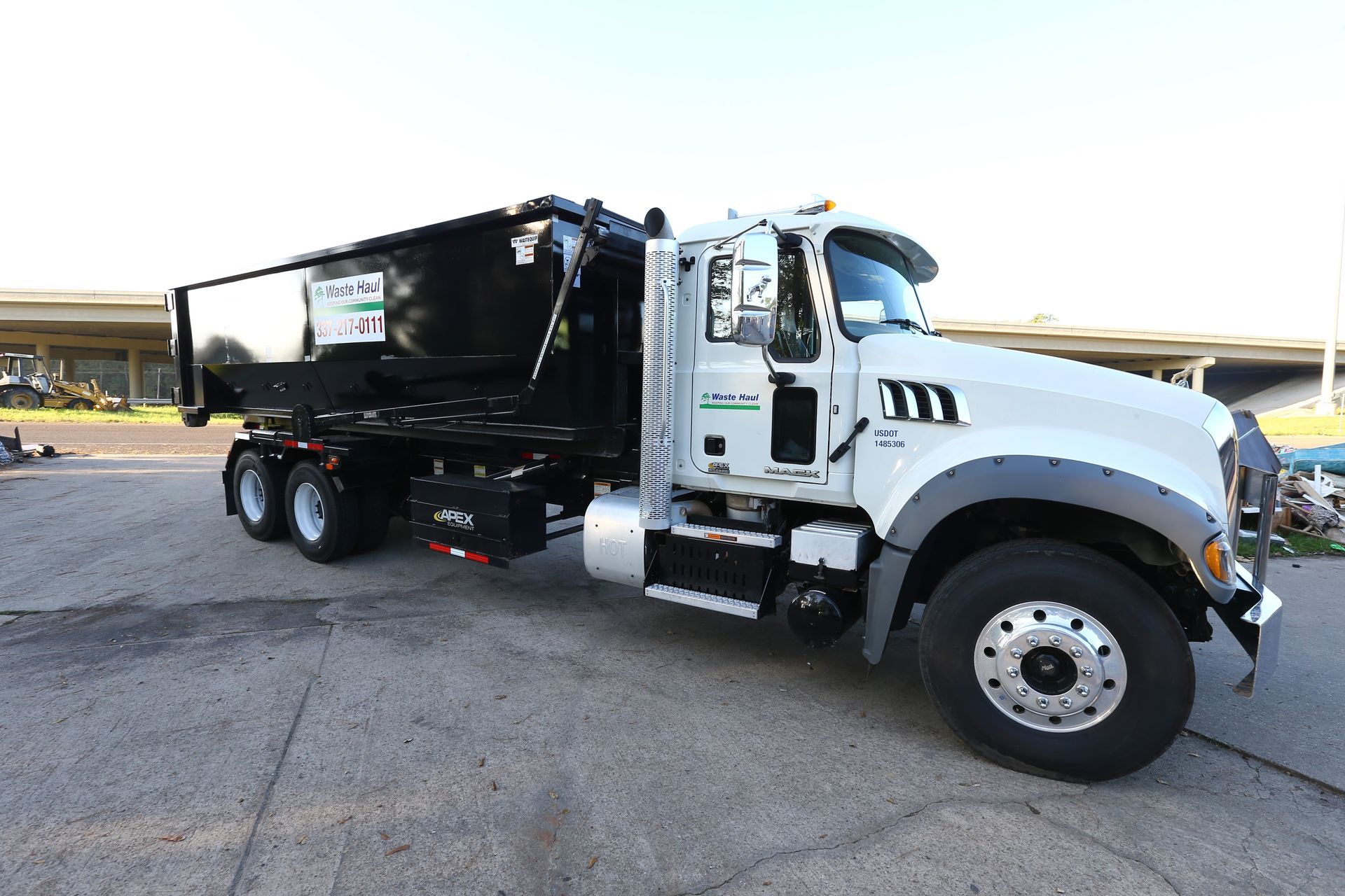 White dump truck parked on a lot, side view with black cargo bed and yellow construction equipment in the background