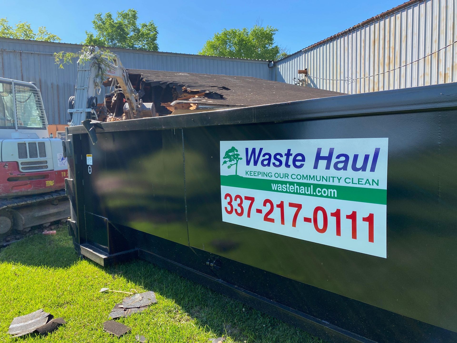 Black Waste Haul dumpster in a yard, with debris inside and company sign on the side.