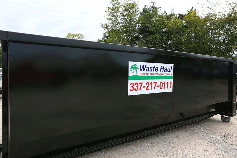 Black Waste Haul dumpster with white and red company sign on a gravel lot