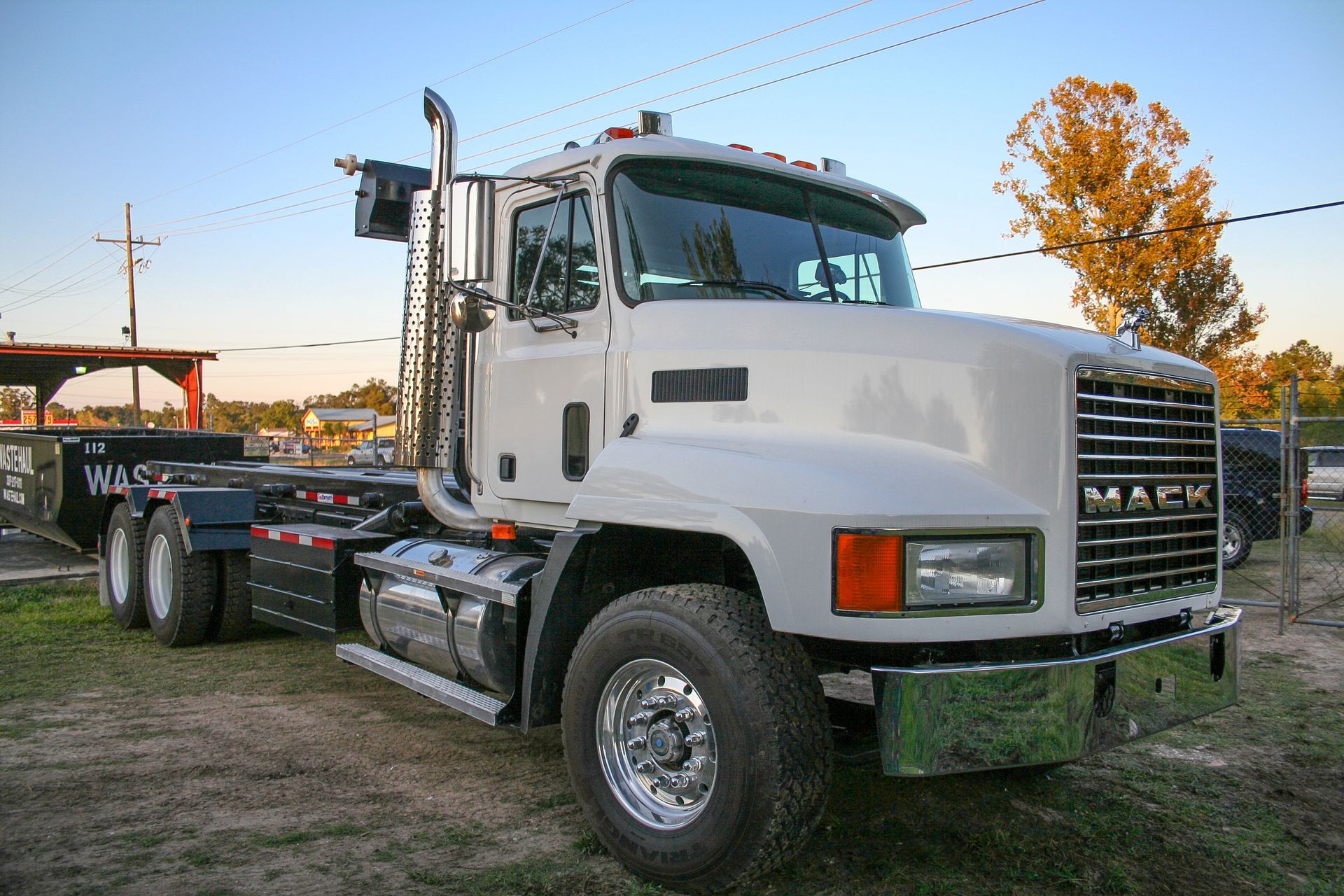 White Mack semi-truck parked outdoors at sunset, viewed from the front-left side.