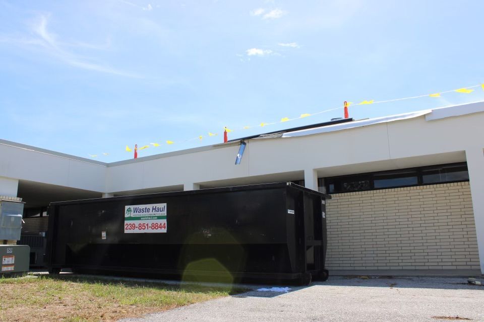 Black dumpster beside a light-colored building with a garage door and parking lot