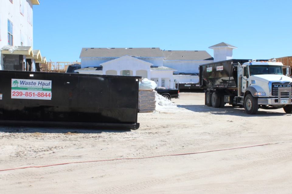 Construction site with a large black dumpster and a truck on a sunny day