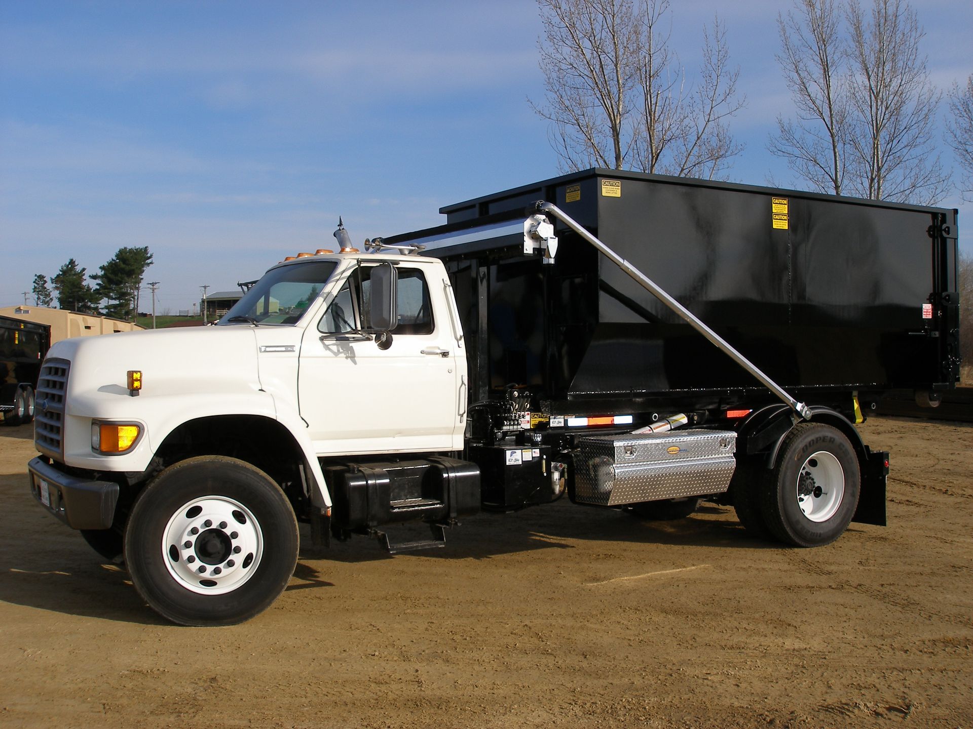 White dump truck with black bed parked on dirt under a blue sky