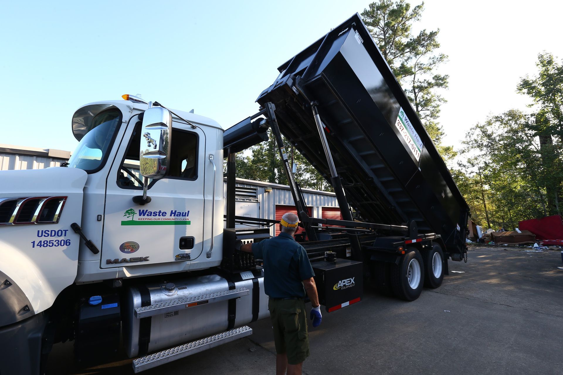Dump truck with raised bed and a worker standing beside it on a roadside.