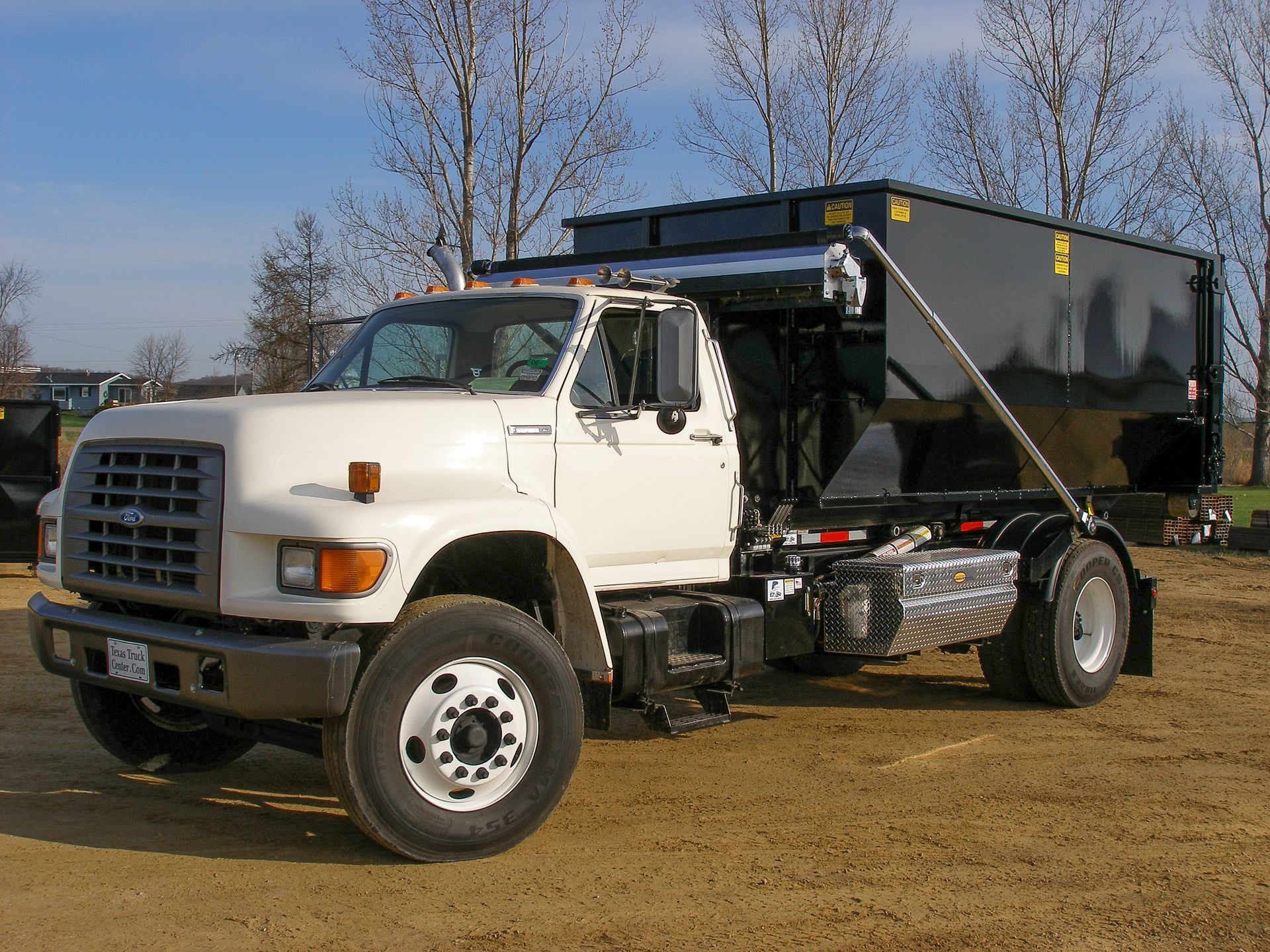 White dump truck with black cargo bed parked on a grassy field under a blue sky