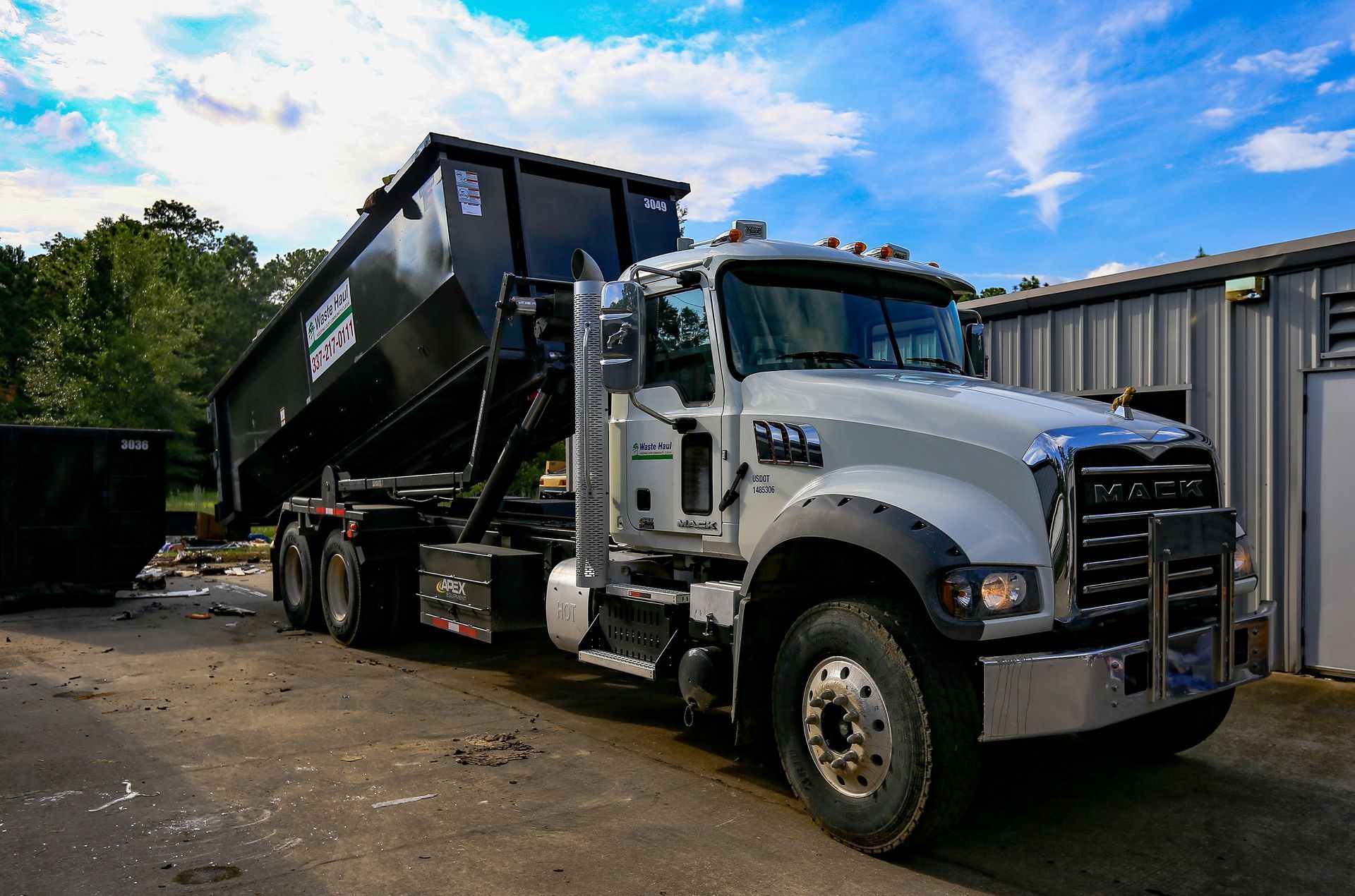 White dump truck with raised black bed parked in a lot under a blue sky