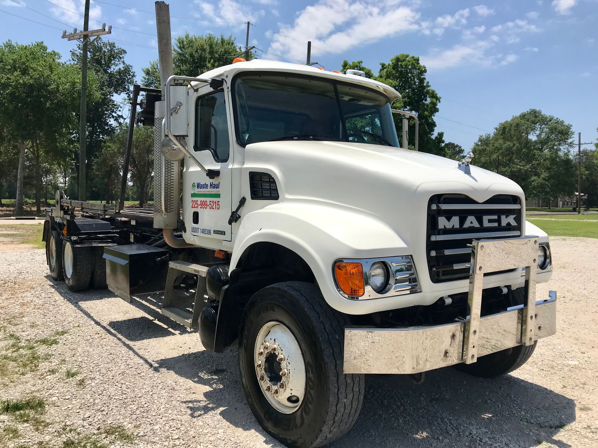 White Mack flatbed truck parked on a gravel lot under a bright blue sky
