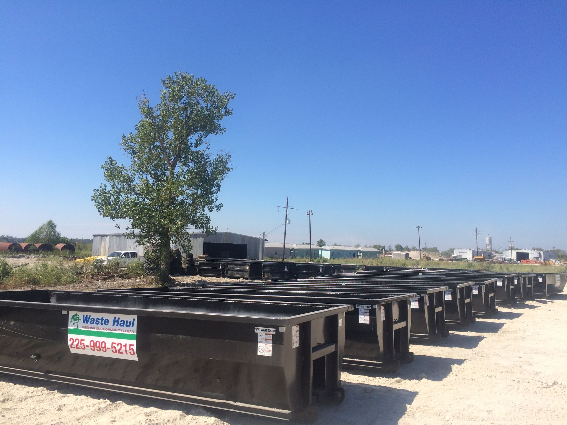 Rows of black metal containers in a dusty outdoor lot under a clear blue sky