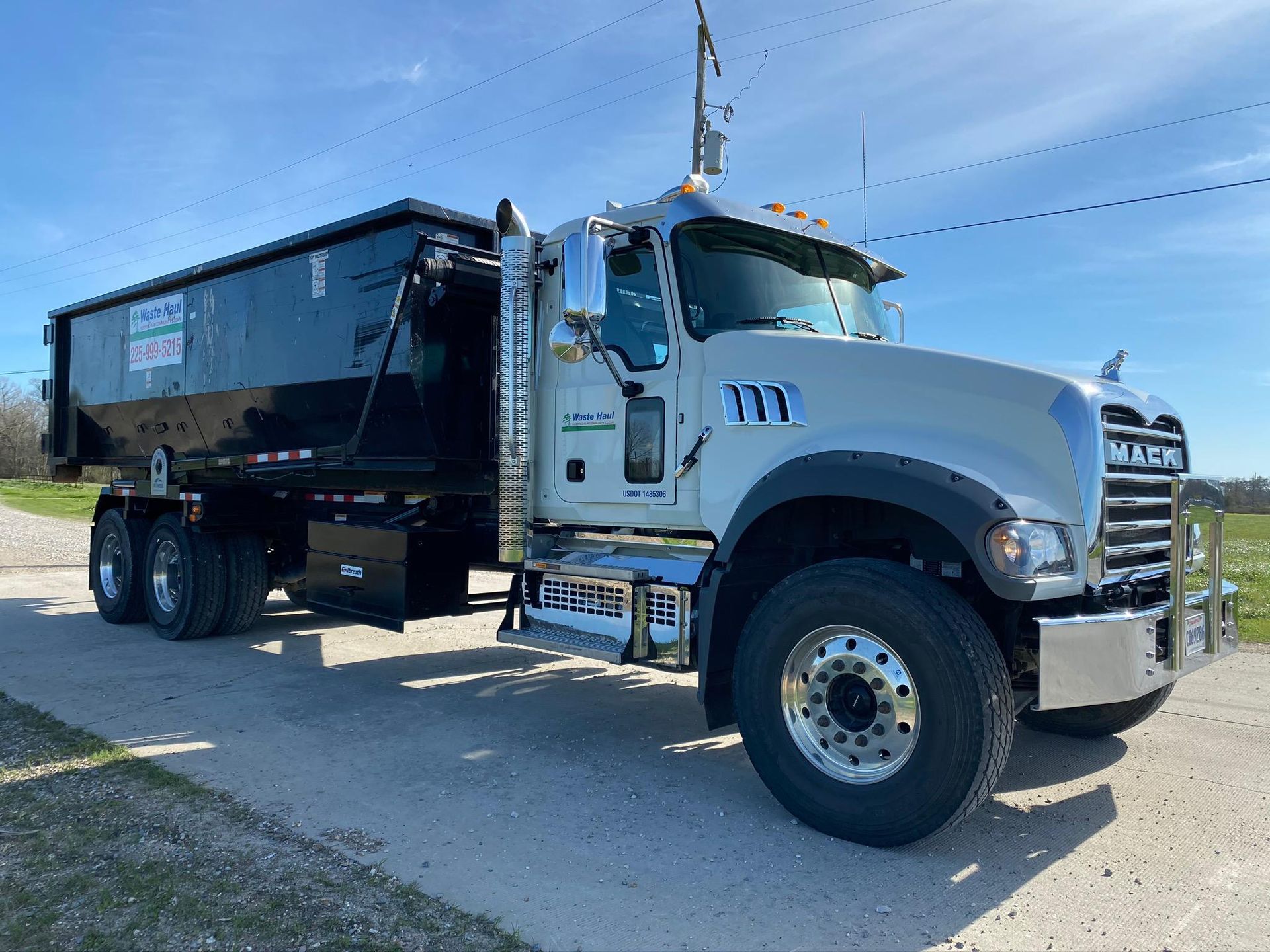 White semi-truck with black dump trailer parked on a gravel lot under a clear sky