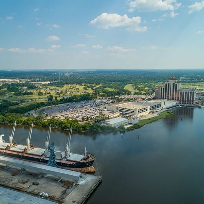 Aerial view of a waterfront port with ships, a parking lot, and industrial buildings beside calm water
