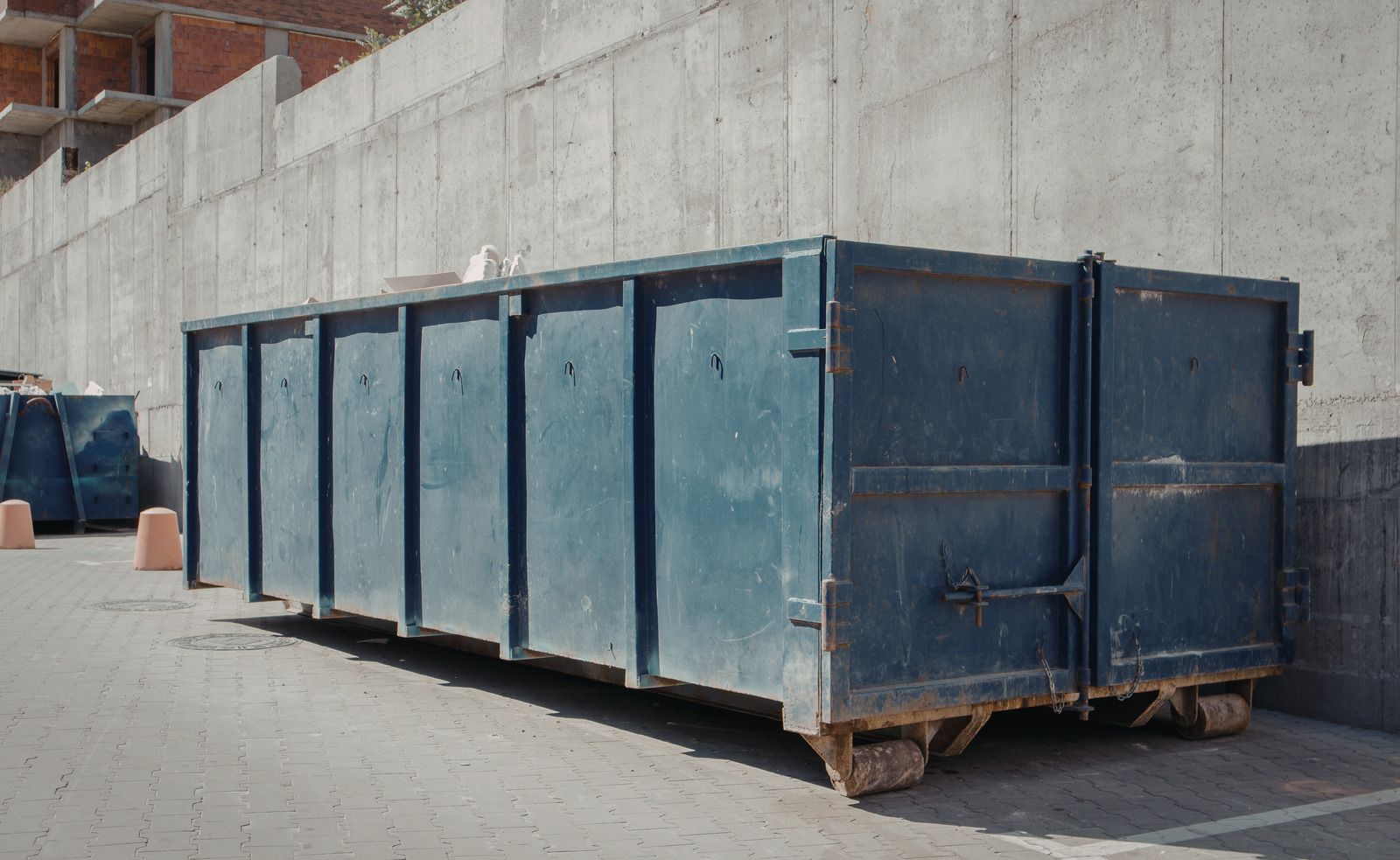 Black metal dumpster in a barren lot under a blue sky