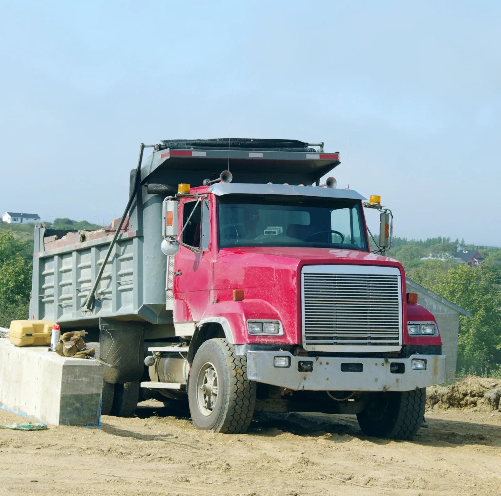 Red dump truck parked on a dirt road beside a concrete barrier under a clear sky