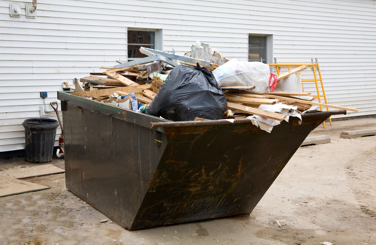 Large construction dumpster filled with wood debris and trash beside a white building