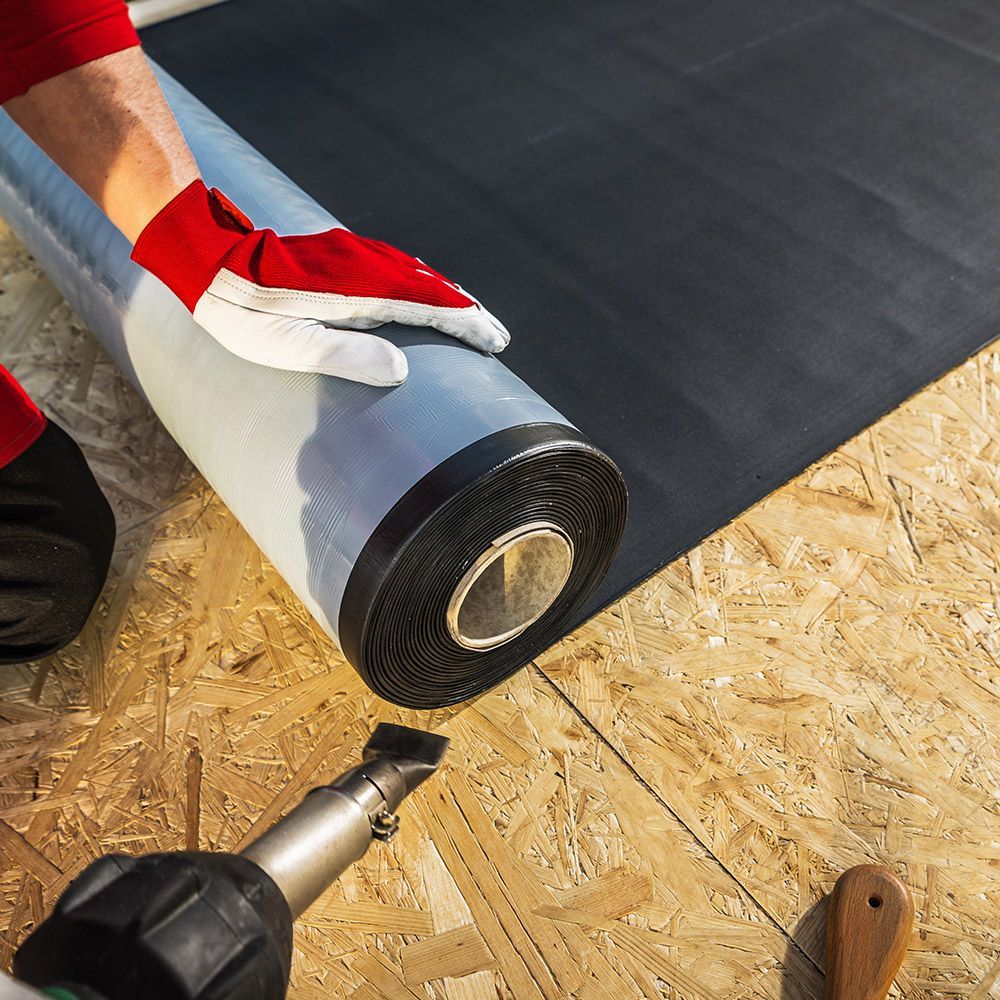 A person wearing red gloves is holding a roll of roofing material.