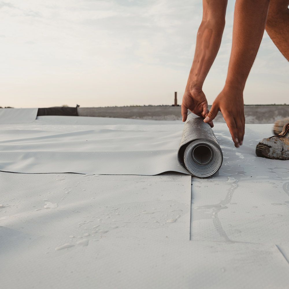 A person is rolling a roll of roofing material on a roof.