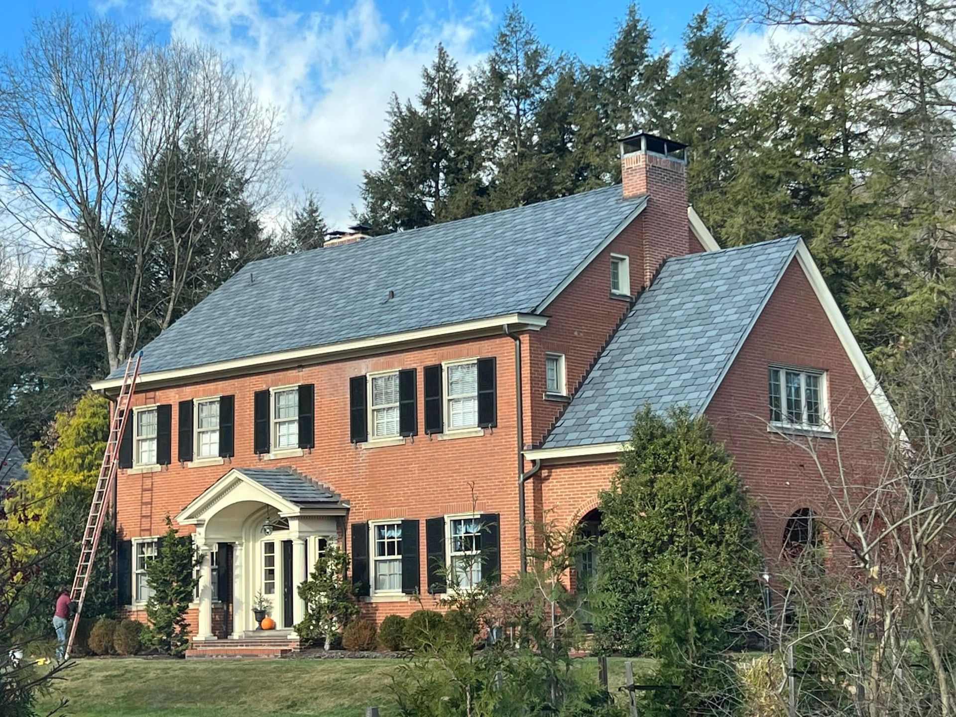 A large brick house with a gray roof is surrounded by trees.