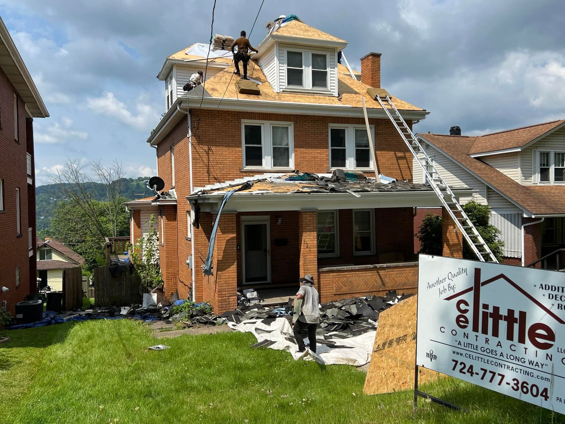 A brick house is being remodeled with a sign in front of it.
