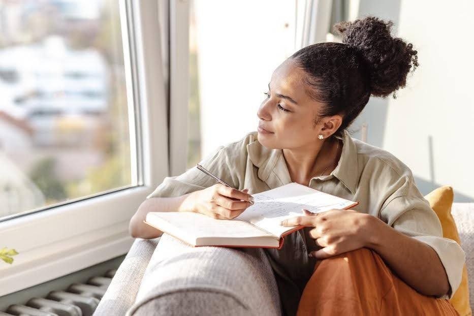 A woman is sitting on a couch writing in a notebook.