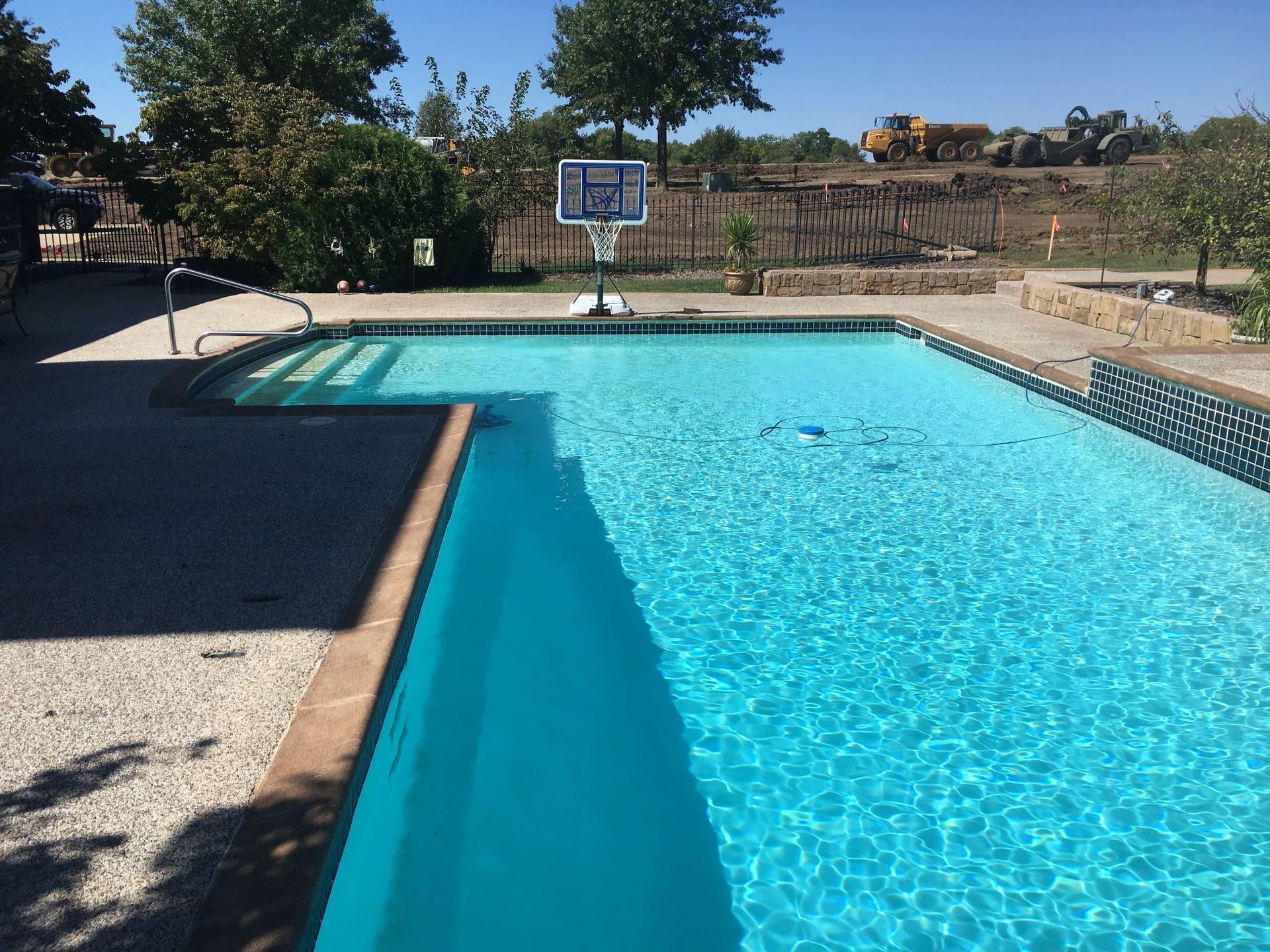 Outdoor swimming pool with clear blue water, dive board, and trees in the background