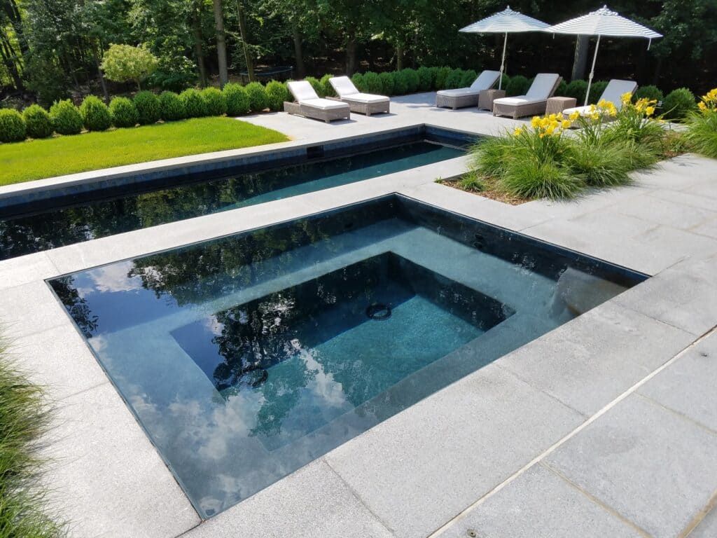 Modern backyard with a small square pool, white loungers, umbrellas, and green landscaping