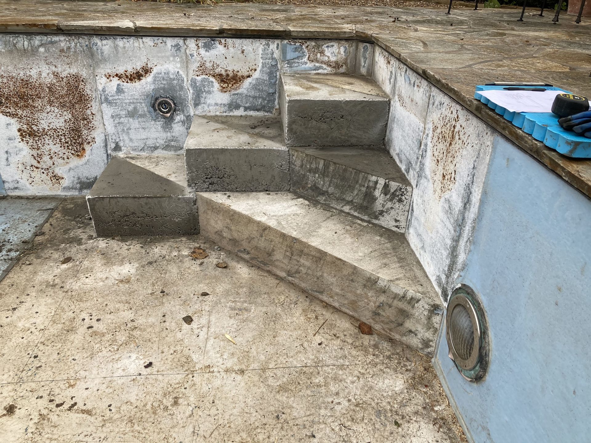 Empty concrete pool with stained walls and built-in steps at one end