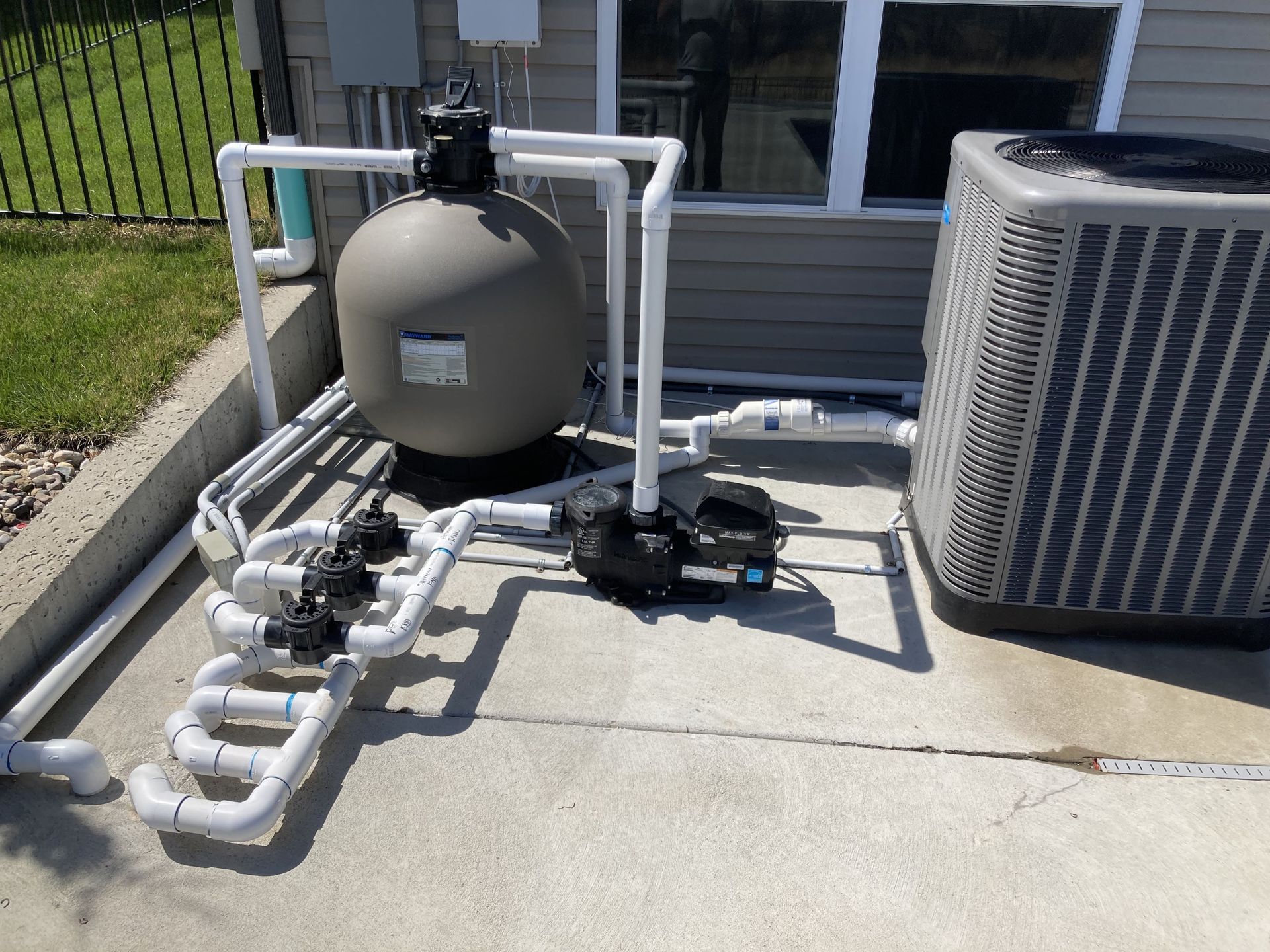 Pool equipment with pipes, pump, filter tank, and air conditioner unit beside a house