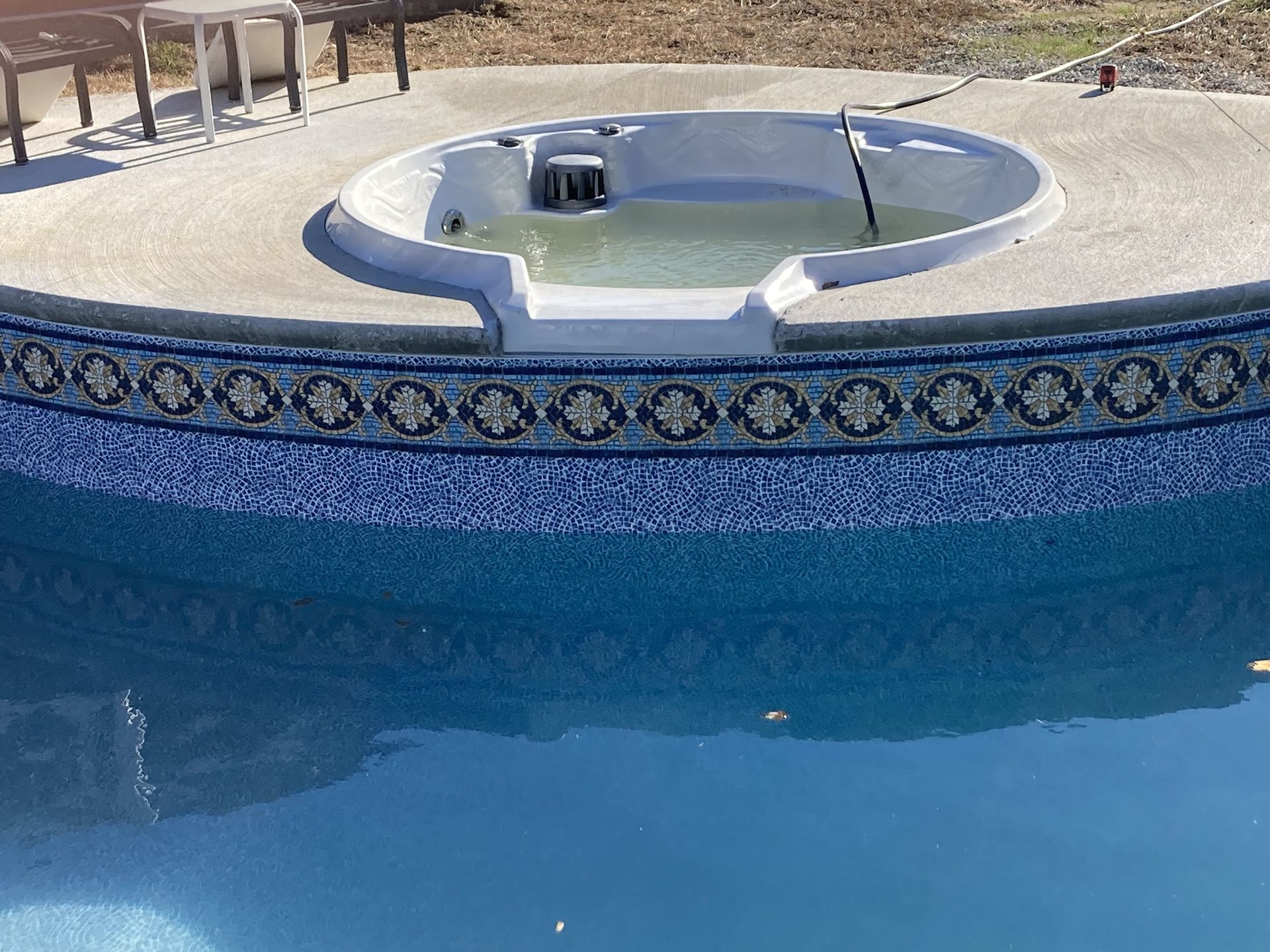 Blue swimming pool with a circular hot tub inset and decorative tile border