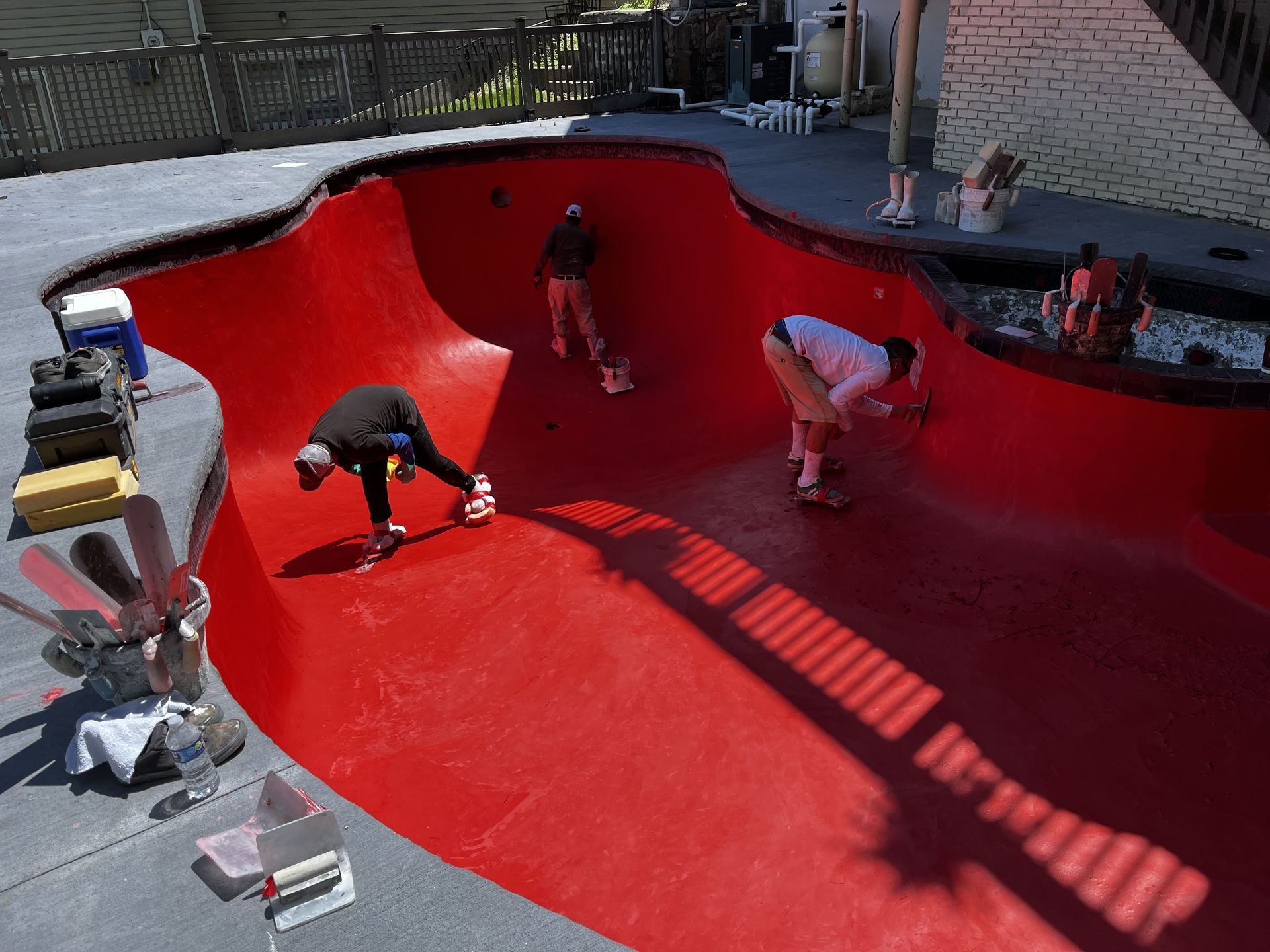 People painting a bright red empty swimming pool with rollers and buckets