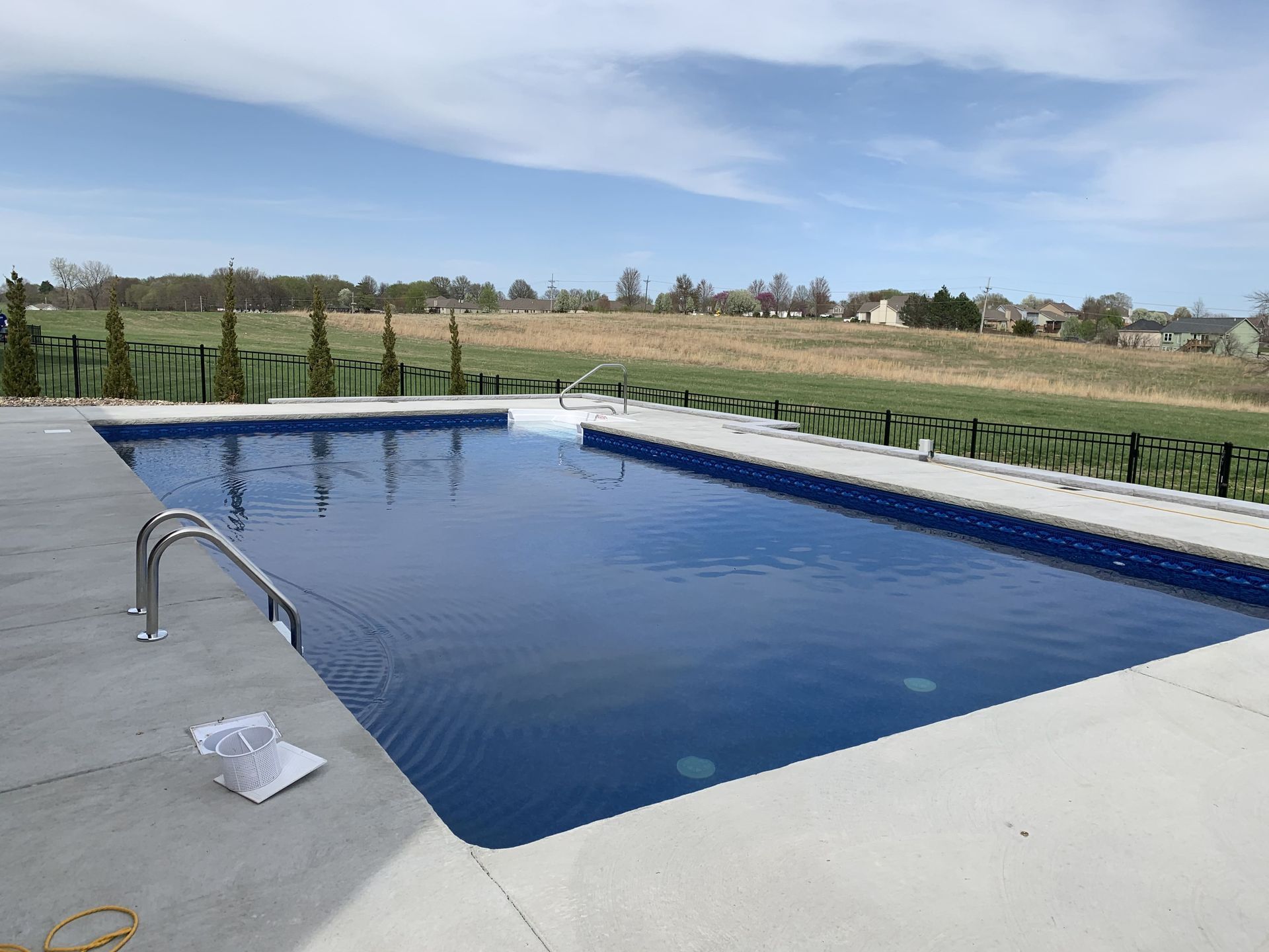Rectangular outdoor swimming pool with blue water beside a concrete deck and grassy field.