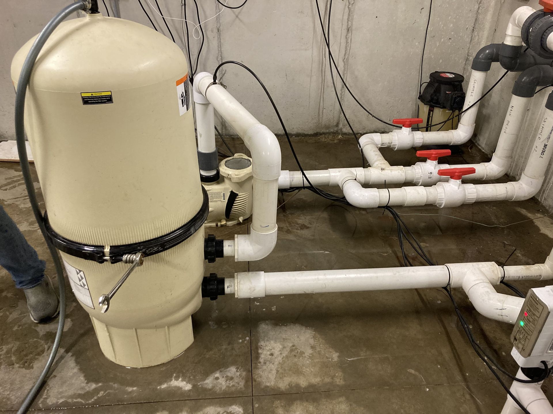 Industrial piping and a beige tank in a utility room with a wet concrete floor