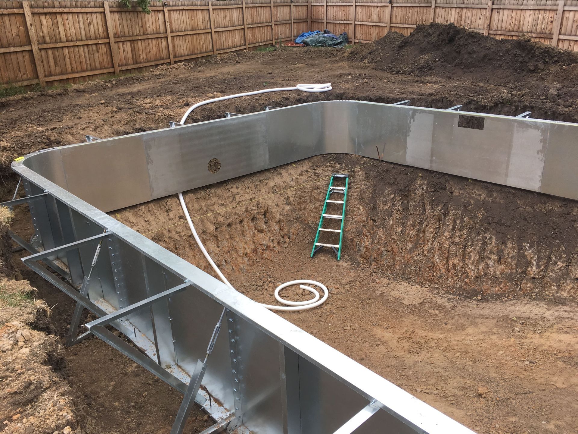 In-ground pool under construction with concrete walls, dirt floor, and a ladder inside.