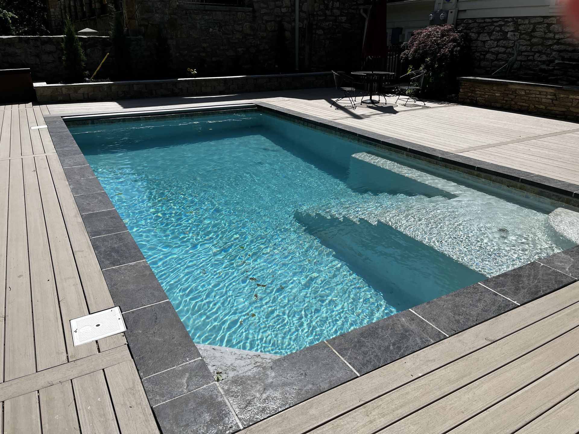 Rectangular outdoor swimming pool with blue water, light stone deck, and built-in steps.