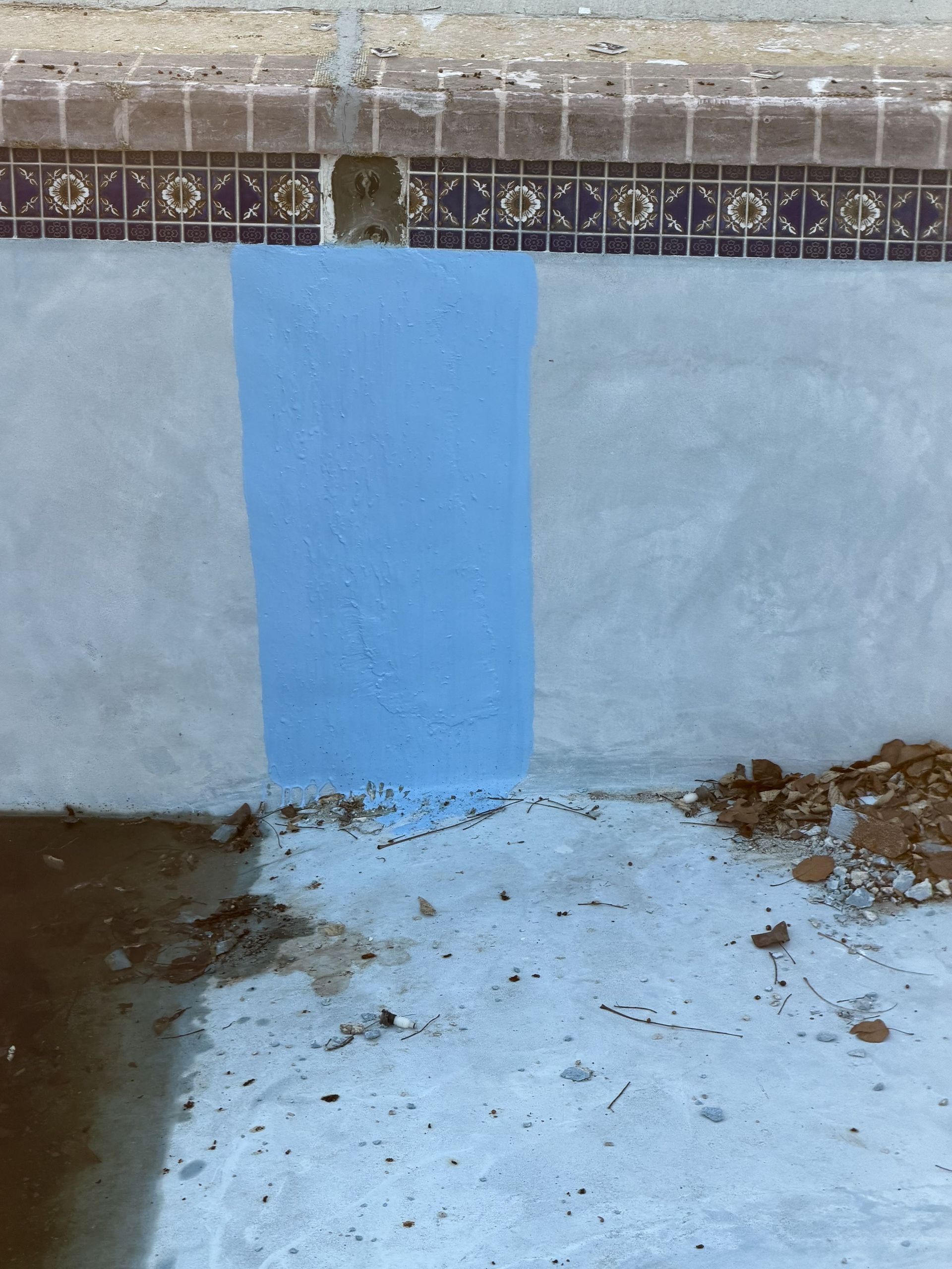 Blue painted patch on a wall above a light concrete floor with dirt and debris nearby.