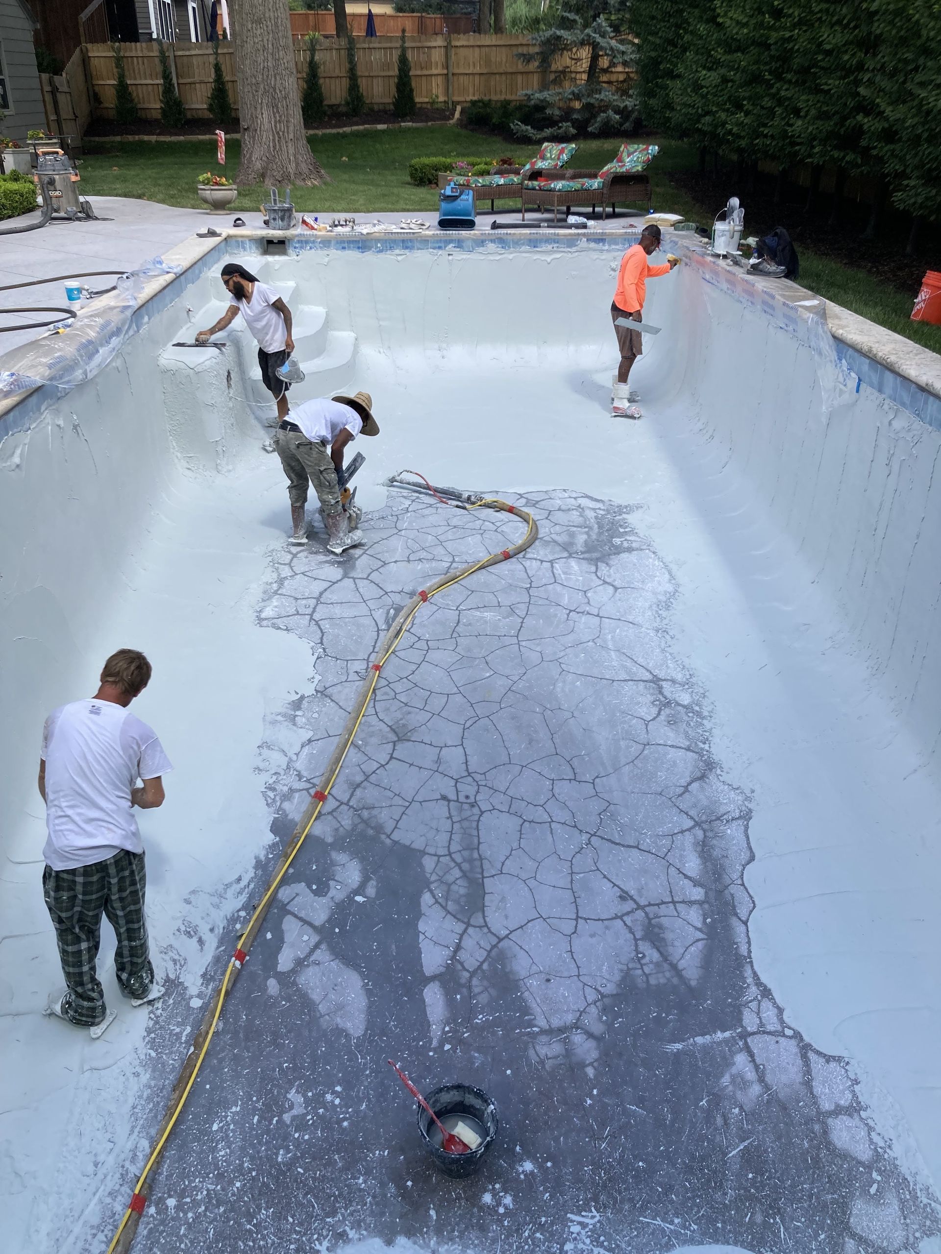 People cleaning a drained swimming pool with hoses and tools outdoors
