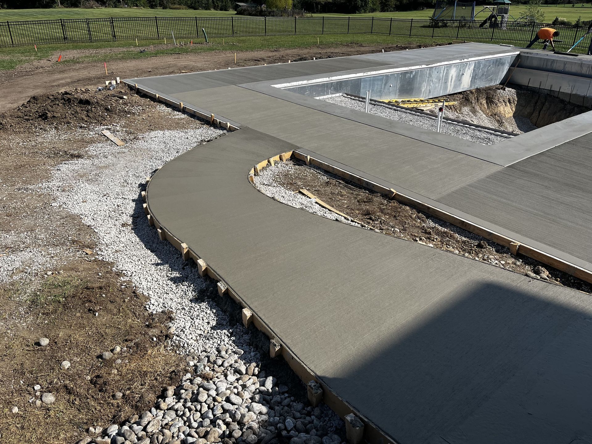 Curved concrete walkway beside a newly built retaining wall and gravel path in a landscaped area