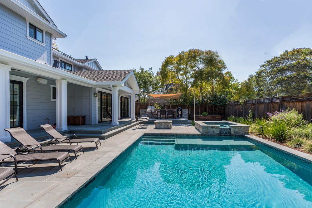 Backyard pool beside a house patio with lounge chairs and a hot tub